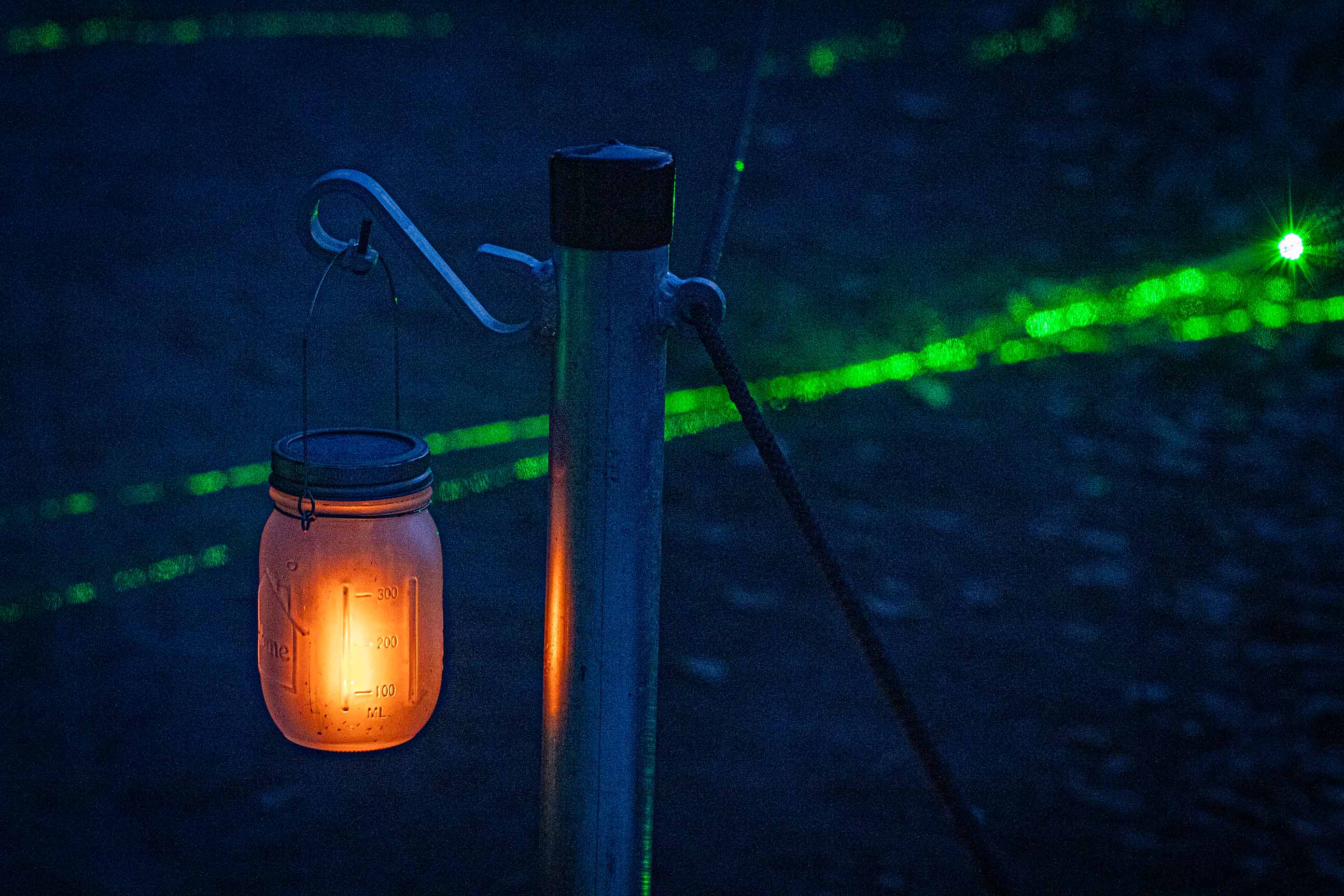 Mason-jar lantern glowing with green light trails at night